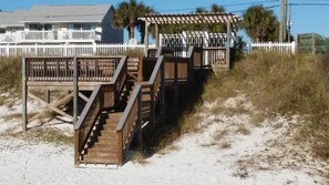 A wooden staircase leading to a beach house with a white fence and palm trees in the background. - Ocean Sky #1604 Closest Beach Access 2-Bd 2-Bath 2nd Floor (Destin)
