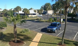 Un estacionamiento con un SUV azul, palmeras y un edificio de techo blanco al fondo.