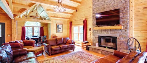 A log cabin interior with a fireplace, leather sofas, and a stone wall.