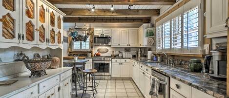 A spacious kitchen with white cabinets, a central island, and a wooden ceiling.