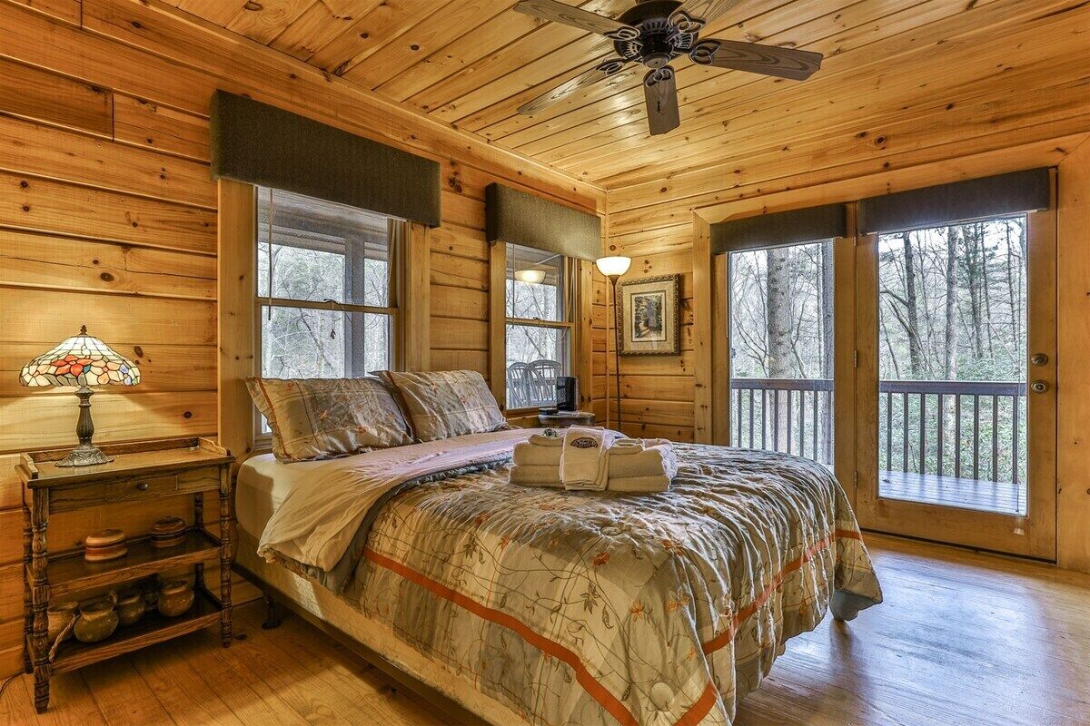 A wooden cabin bedroom with a bed, a nightstand, a lamp, and a ceiling fan.