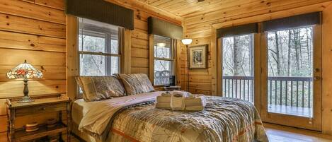 A wooden cabin bedroom with a bed, a nightstand, a lamp, and a ceiling fan.