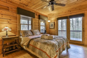A wooden cabin bedroom with a bed, a nightstand, a lamp, and a ceiling fan.