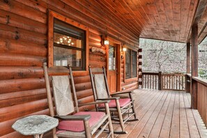 A log cabin with a porch, rocking chairs, and a wooden table.