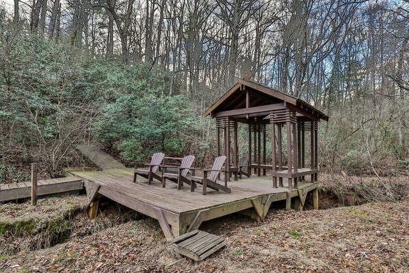 A wooden deck with chairs and a gazebo in a forested area.