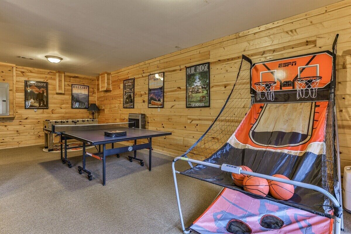 A room with a ping pong table, a basketball hoop, and posters on the walls.