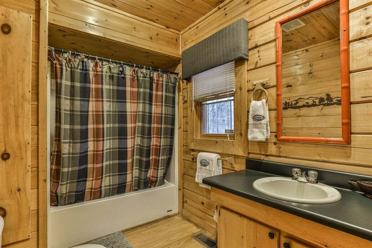 Une salle de bain rustique, avec des murs en bois, une douche ornée d’un rideau à carreaux, un lavabo et un miroir avec un cadre orange.