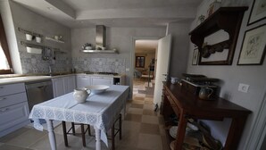 Una cocina con armarios blancos, salpicadero de azulejos, una mesa de comedor con mantel estampado y un aparador de madera con vajilla.