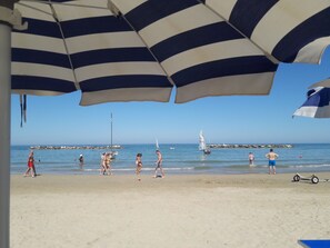 A beach scene with people walking and a sailboat in the water. - Casale Caldarette historic exclusive country house (Ponte Ete-Caldarette)