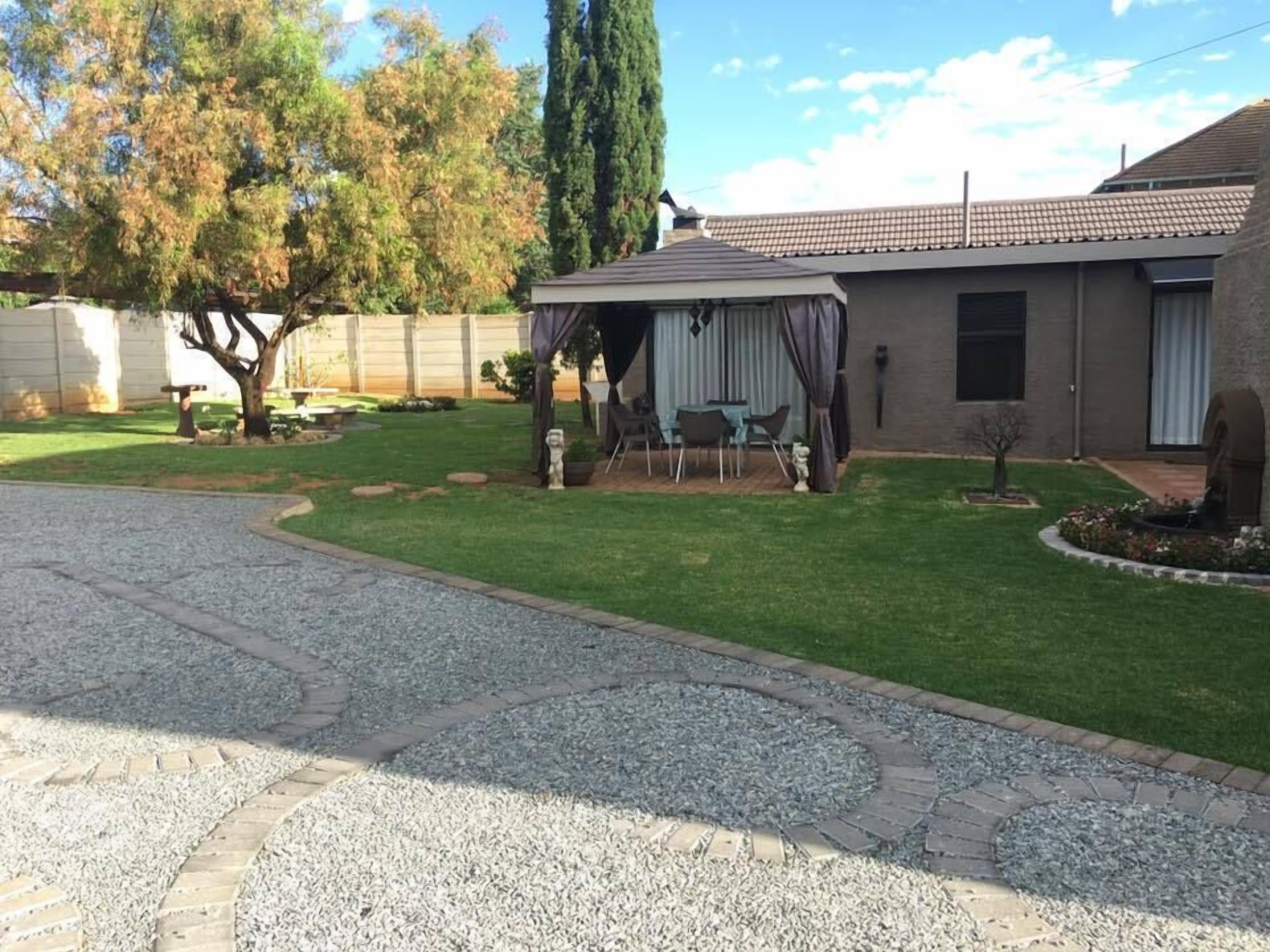 Una propiedad residencial con un césped cuidado, un patio con mobiliario exterior, una zona de estar cubierta y un camino de ladrillo que lleva a la casa.