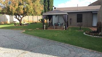 Una propiedad residencial con un césped cuidado, un patio con mobiliario exterior, una zona de estar cubierta y un camino de ladrillo que lleva a la casa.
