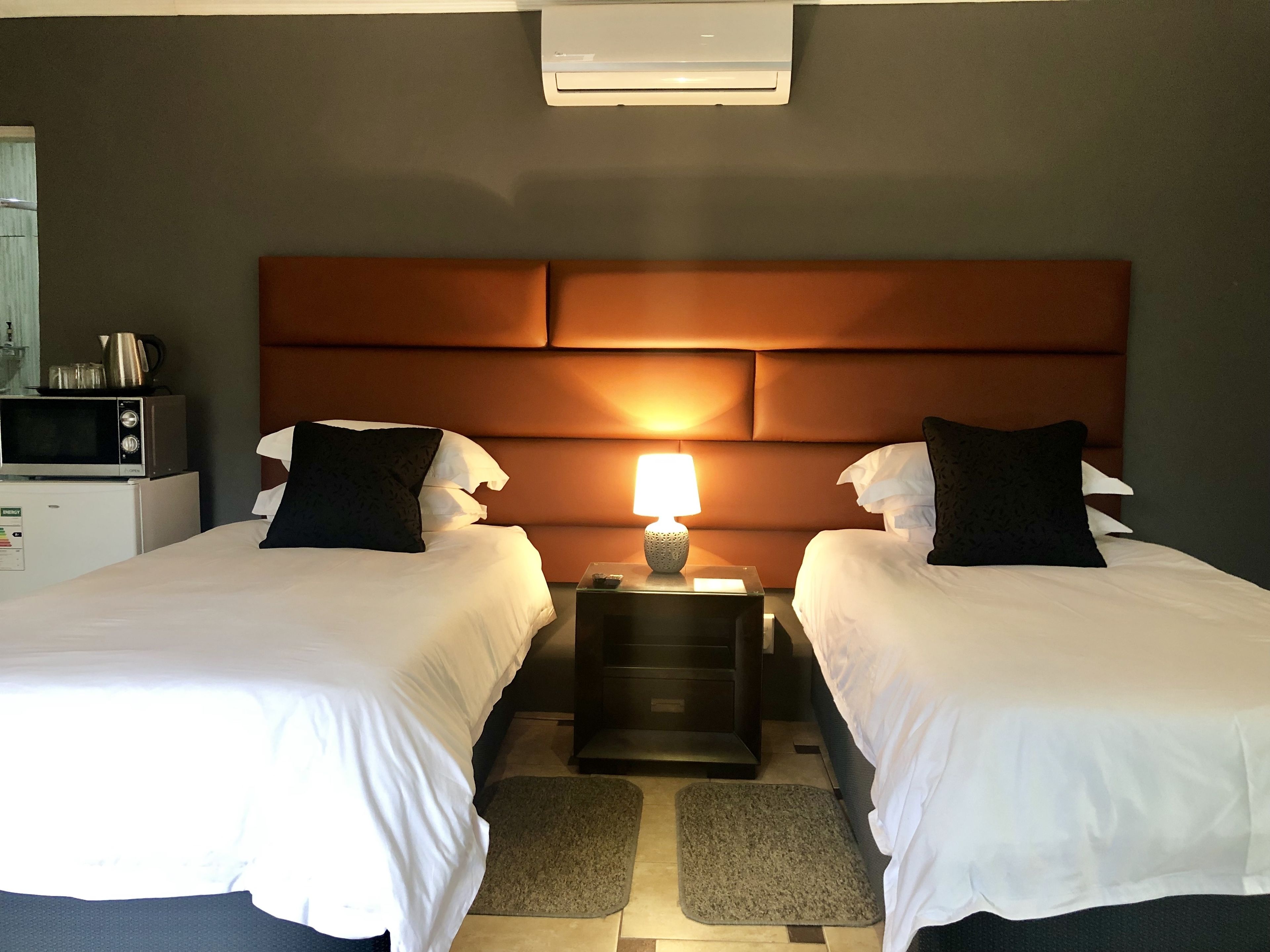 Una habitación de hotel con dos camas, una mesita de noche con lámpara, microondas y refrigerador.