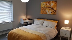 A bedroom with a bed, a desk, a chair, a radiator, and a wall-mounted painting.