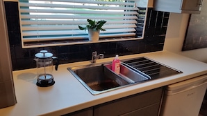 A modern kitchen with a stainless steel sink, a coffee maker, and a potted plant on the window sill.