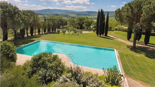 A rectangular swimming pool with a clear blue water surface, surrounded by a well-maintained lawn and tall trees.