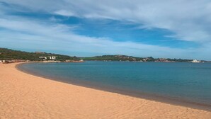 A wide sandy beach with calm waters, a few boats, and buildings in the background.