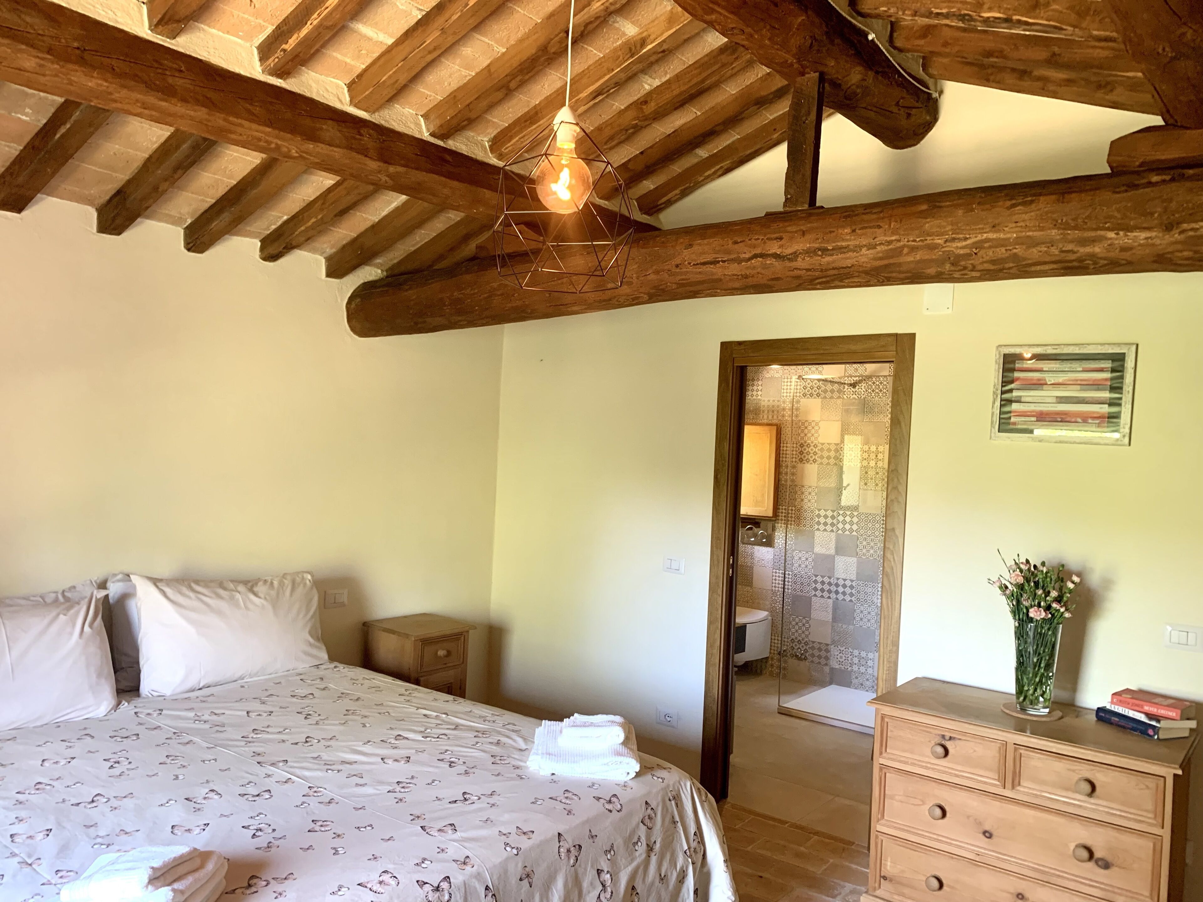 Un dormitorio con cama, vigas de madera, cómoda, espejo y zona de ducha.