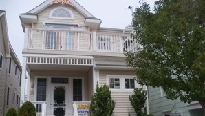 A two-story house with a front porch, a small balcony, and a sign indicating it is for sale.