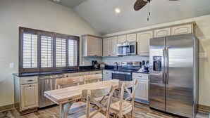 A kitchen with a dining table, chairs, stainless steel appliances, and a ceiling fan.