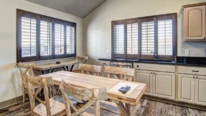 A kitchen with wooden cabinets, a dining table with chairs, and large windows with blinds.