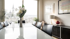 Een vergaderruimte met een grote tafel, stoelen, een vaas met bloemen, een lamp en lijstjes met foto's aan de muur.