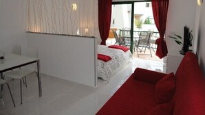 A room with a bed, a red sofa, a dining table, and a ceiling fan. - Bright studio in Tenerife, with terrace, pool, internet wi-fi fiber (Adeje)