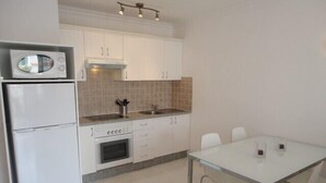 A compact kitchen with white cabinets, a microwave, an oven, and a dining area with a table and chairs. - Bright studio in Tenerife, with terrace, pool, internet wi-fi fiber (Adeje)