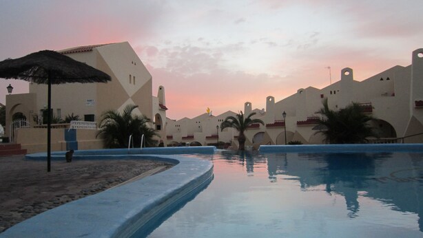 A resort pool area with a sunset sky, palm trees, and a building with a unique architectural design. - Bright studio in Tenerife, with terrace, pool, internet wi-fi fiber (Adeje)