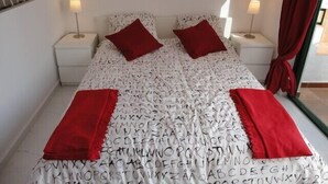 A neatly made bed with alphabet-patterned bedding, two red pillows, and two bedside lamps. - Bright studio in Tenerife, with terrace, pool, internet wi-fi fiber (Adeje)