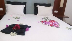 A neatly made bed with white sheets, two black pillows, and a floral arrangement on the left side. - Hotel Limeira (Cidade Velha)