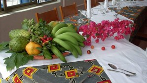 A table set for a meal with a patterned tablecloth, fruit, flowers, and white candles. - Hotel Limeira (Cidade Velha)