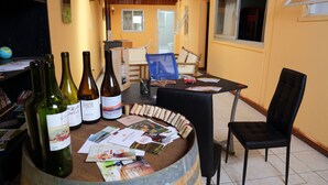 Espaço para degustação de vinhos com várias garrafas e rolhas dispostas sobre uma mesa, rodeado por cadeiras e um barril de madeira.