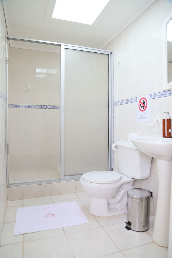 A bathroom with a shower, toilet, sink, and trash can. - Casa Suiza - Hostel (Santa Cruz)