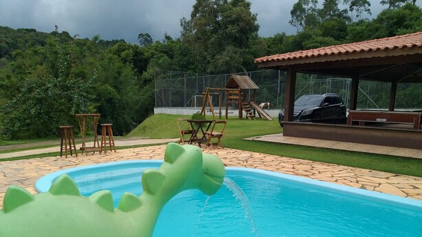 A swimming pool with a green inflatable dinosaur toy, surrounded by a patio area with tables and chairs, and a covered seating area. - Casa Sítio Mairiporã (Mairipora)