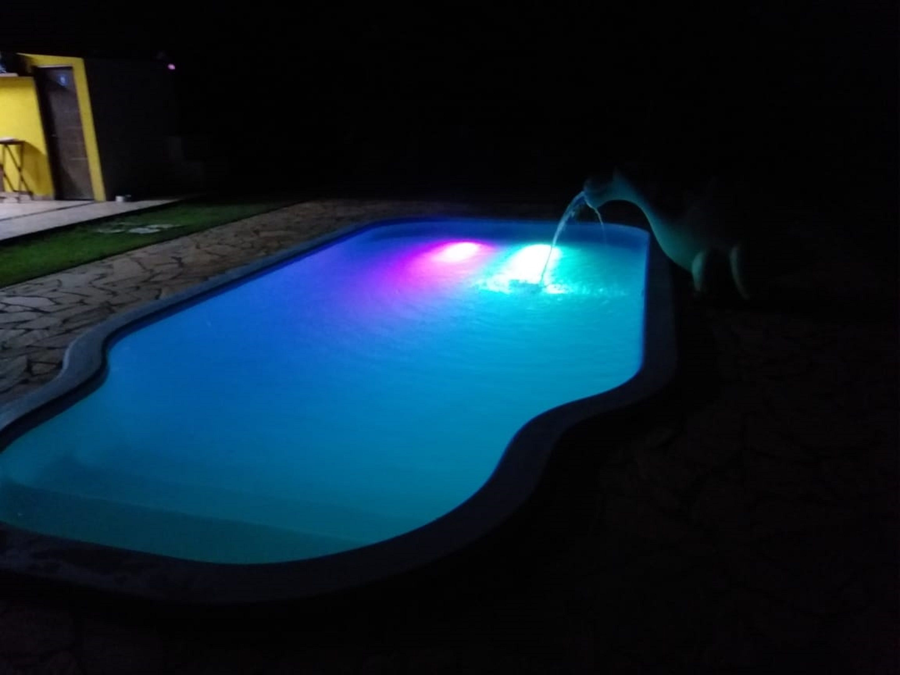 Una piscina con fuente iluminada por la noche.