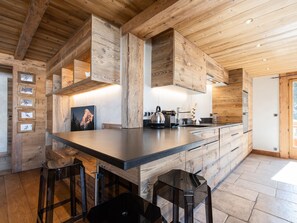 A modern kitchen with wooden cabinetry, a central island, bar stools, and a large window.