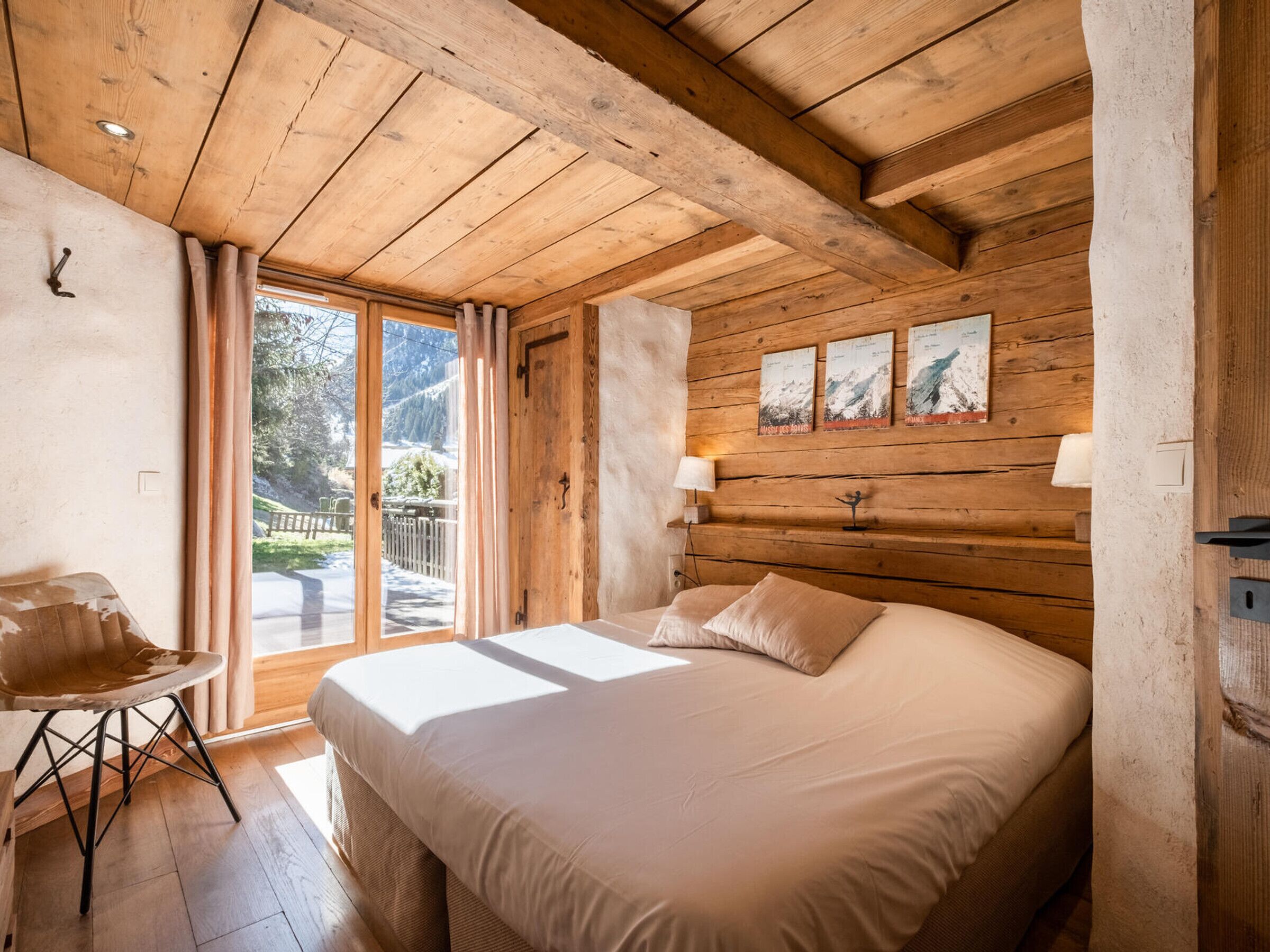 Une chambre aux murs lambrissés, avec un lit, une chaise et une fenêtre donnant sur un balcon.