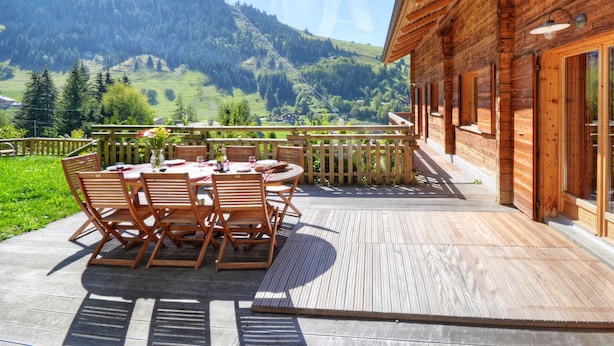 Une terrasse en bois avec une table et des chaises, offrant une vue sur un paysage montagneux.