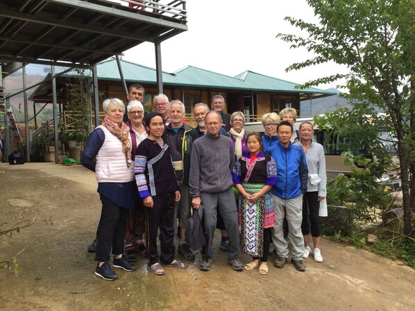 A group of people standing in front of a building with a green roof and wooden structure.