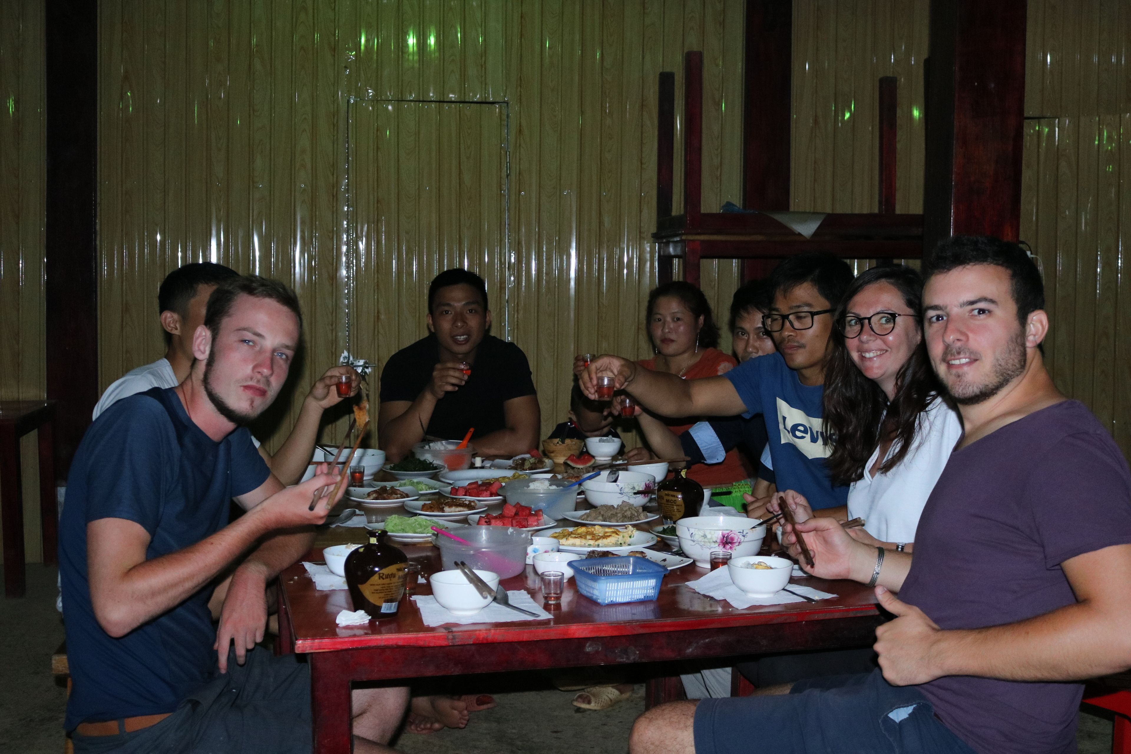 Um grupo de pessoas jantando em uma mesa de madeira, com diversos pratos e bebidas.