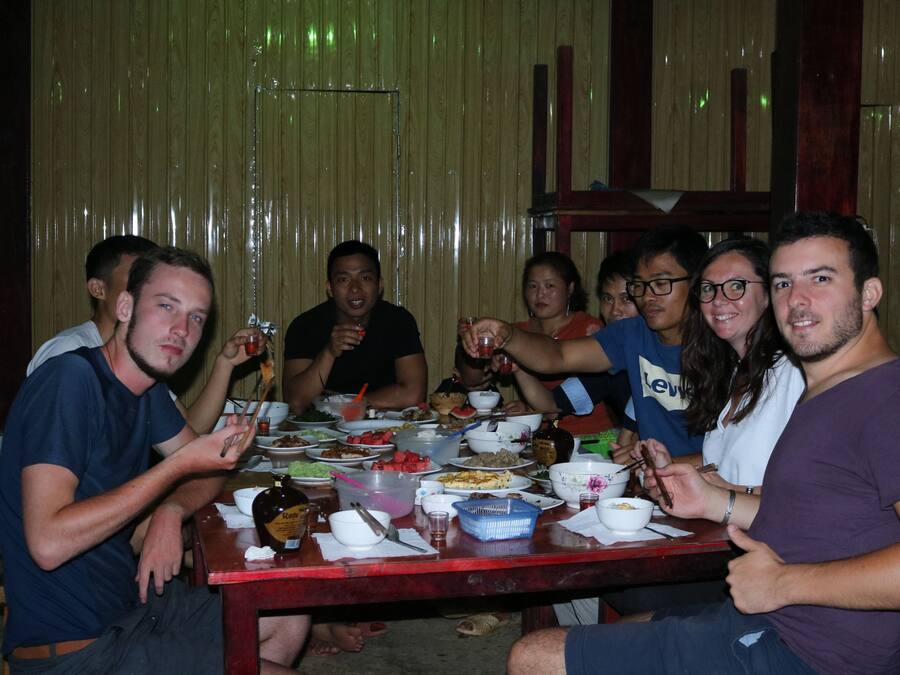Um grupo de pessoas jantando em uma mesa de madeira, com diversos pratos e bebidas.