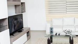 A modern living room with a white sofa, a glass coffee table, and a flat-screen TV on a wooden stand.