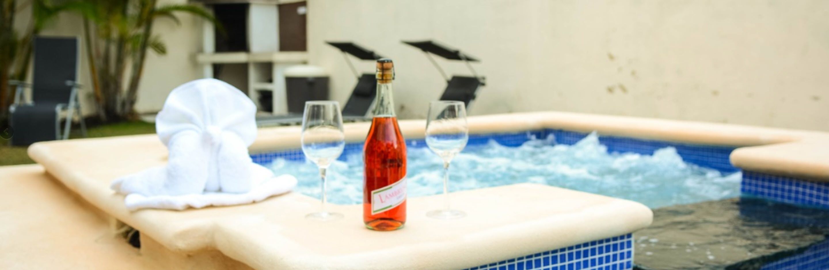 Un jacuzzi con una botella de vino y copas, una toalla y sillones de descanso al fondo.