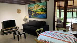 A living room with a TV, sofa, coffee table, and a table with a striped tablecloth.