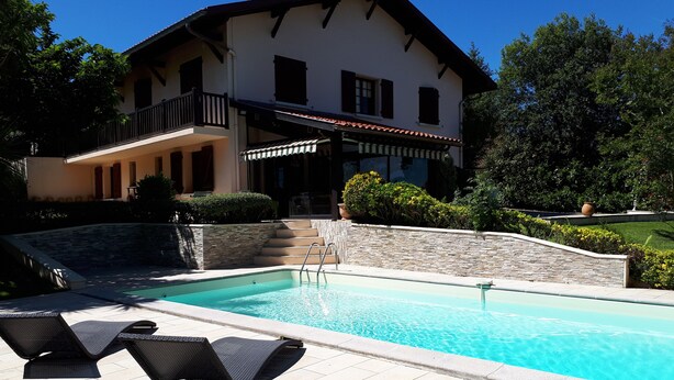 A two-story house with a swimming pool, a covered patio, and a stone retaining wall.