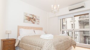 A bedroom with a large bed, a nightstand, a lamp, a chandelier, an air conditioner, and a window with a view of buildings. - Austria apartment by Be Local Argentina (Buenos Aires)