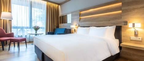 Une chambre d’hôtel moderne avec un grand lit, un bureau, une chaise et une fenêtre avec des rideaux.