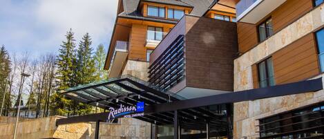 A modern hotel with a stone facade, large windows, and a covered entrance.