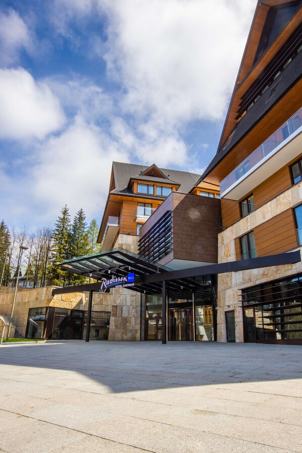 A modern hotel with a stone facade, large windows, and a covered entrance.