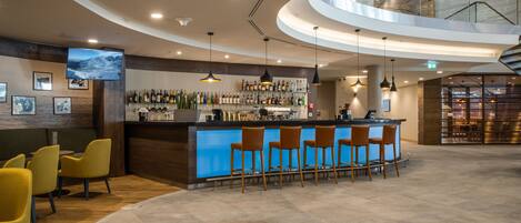 A modern bar area with a curved counter, multiple bar stools, and a variety of bottles.